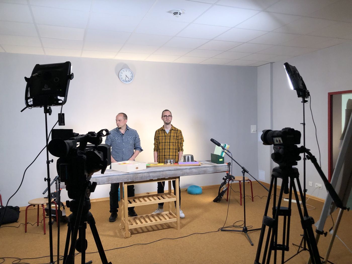 Dreh eines Tutorial-Videos: zwei Personen hinter einem Tisch mit Instrumenten, davor zwei Kameras, Mikrofon und Flächenleuchten